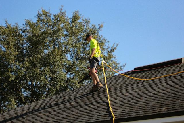 Roofer in a safety harness working on a sloped roof on a sunny day