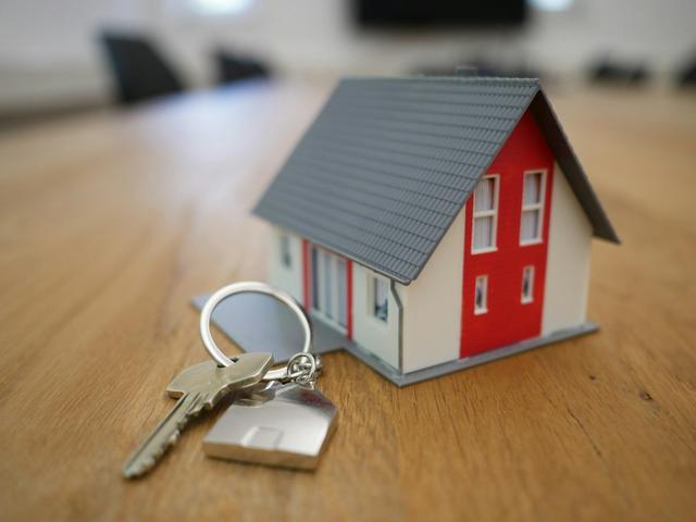 Small model house with a grey roof next to a set of house keys on a table