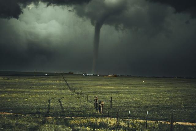 Stormy dark sky with a funnel cloud touching down over a field